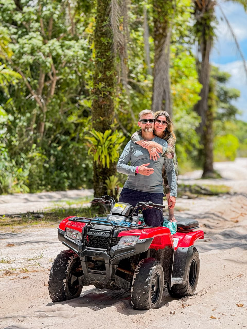 Casal abraçado em um quadriciclo vermelho em trilha de areia