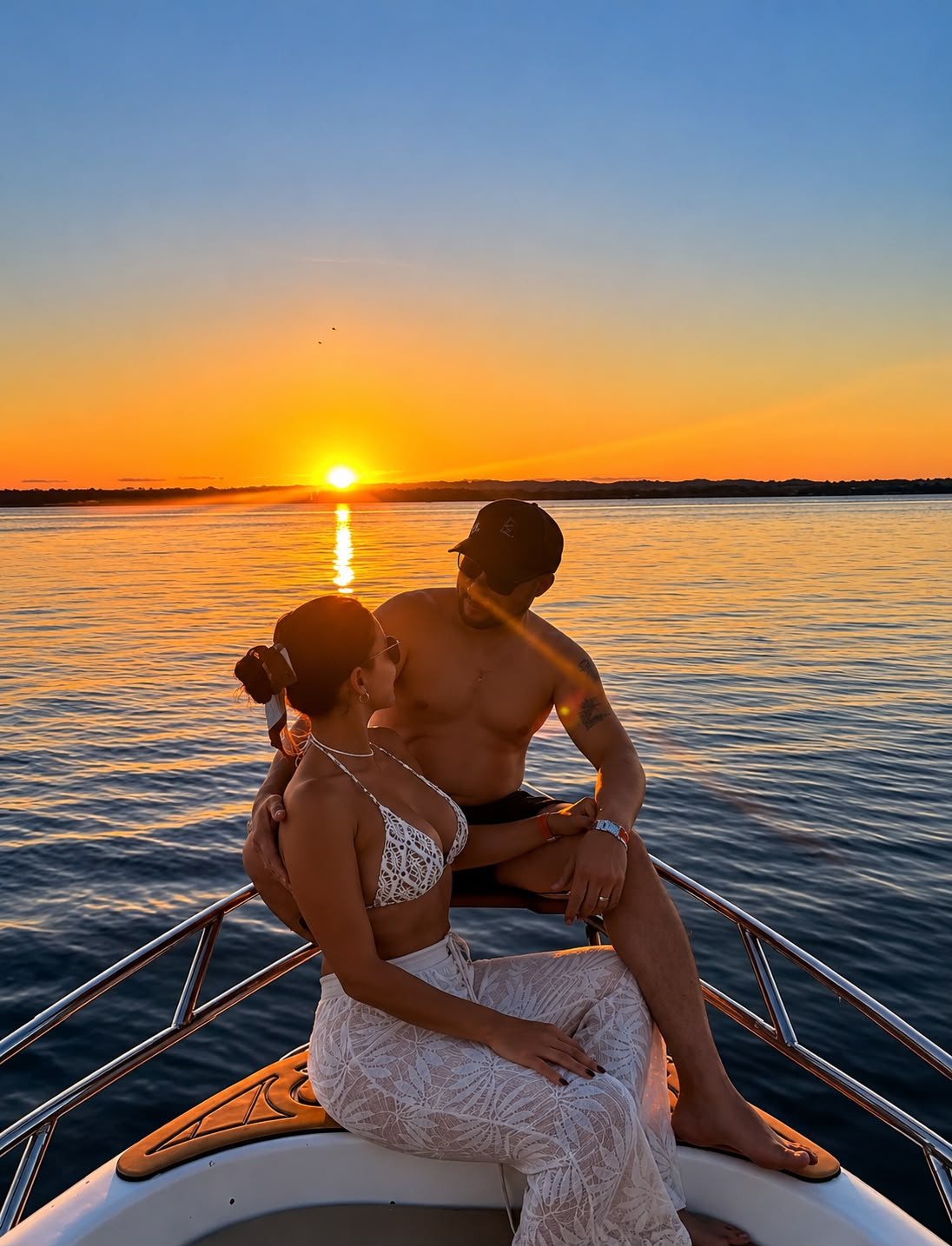 Casal na proa de uma lancha contemplando o pôr do sol no mar