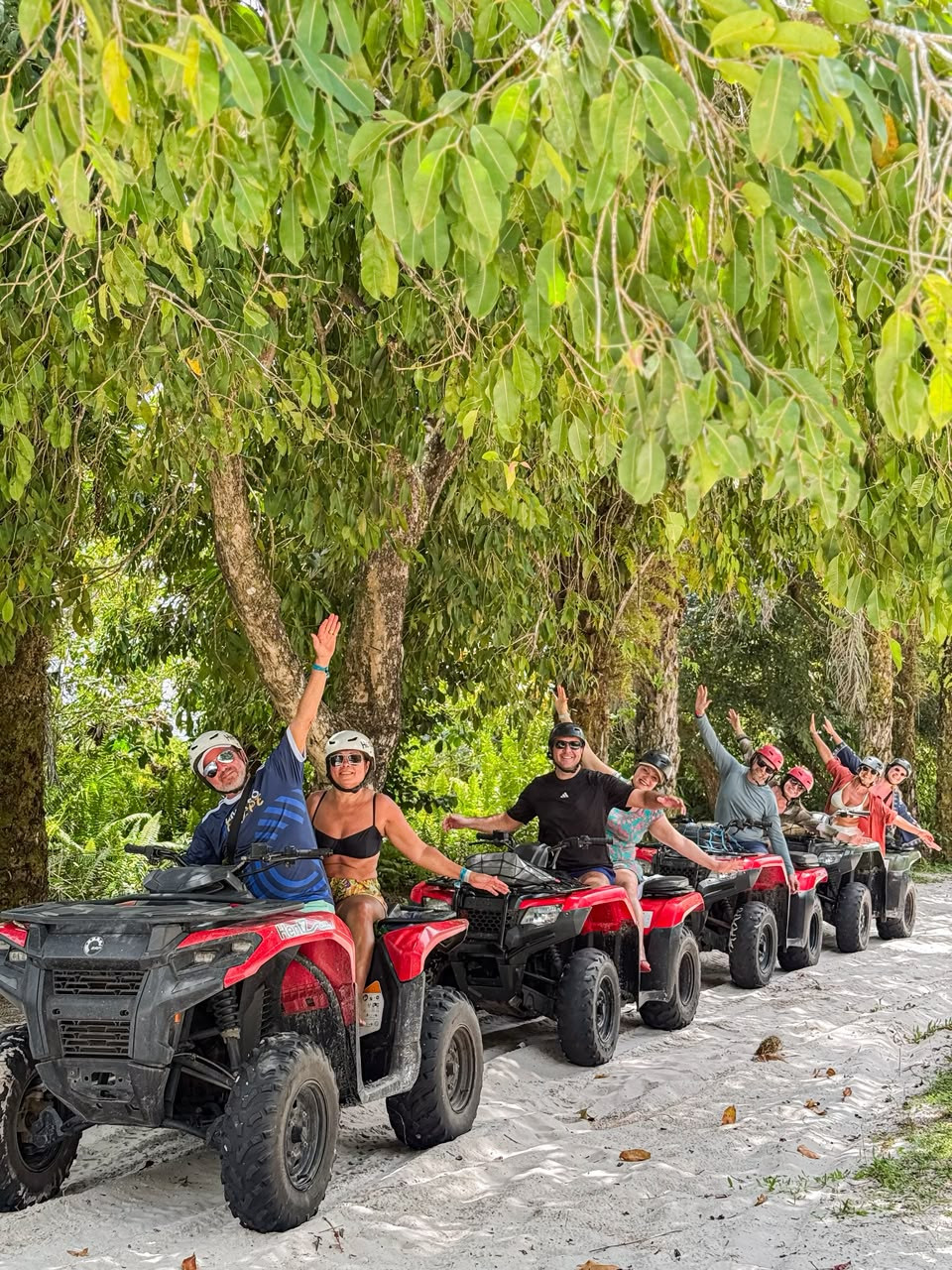 Grupo acenando em comboio de quadriciclos vermelhos por uma trilha de areia sob as árvores